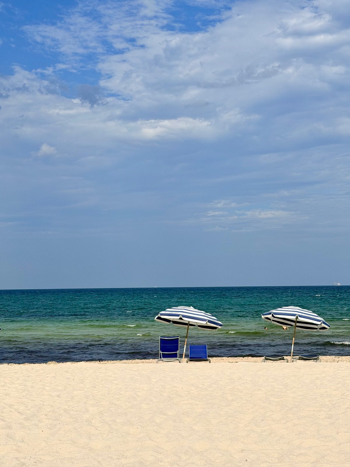 Two blue and white striped beach umbrellas on white sand by a turquoise sea